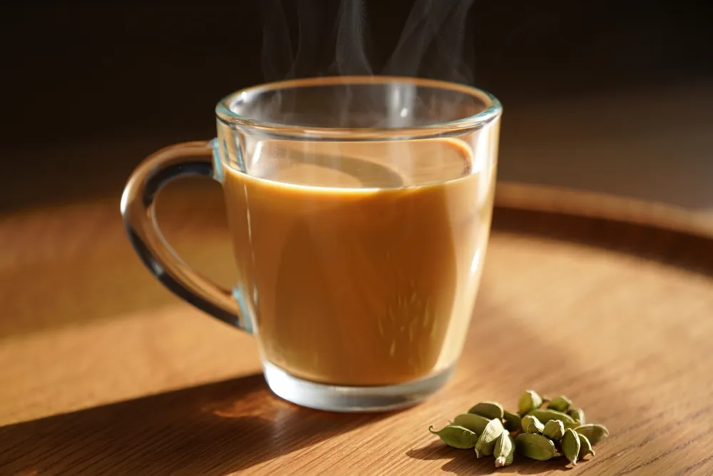 Glass of cardamom chai with cracked green cardamom pods